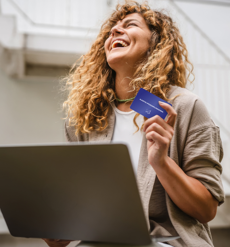 kobieta siedząca przy komputerze i trzymająca kartę podarunkową 